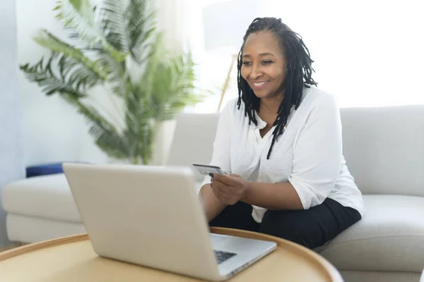Φωτογραφία της όμορφης μαύρης γυναίκας που χρησιμοποιεί φορητό υπολογιστή στο σπίτι καναπέ και να αγοράσει κάτι στο διαδίκτυο — Φωτογραφία Αρχείου