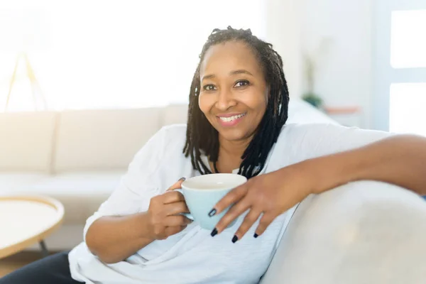 Portrait of an african woman sit on the sofa with coffee — Stockfoto