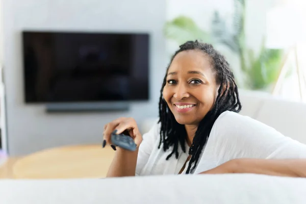 Portrait of an african woman sit on the sofa and holding remote control — Stockfoto