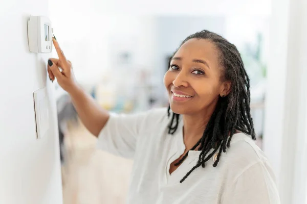 A frican woman lady adjusting the climate control panel on the wall wall thermostat — Stock Photo, Image