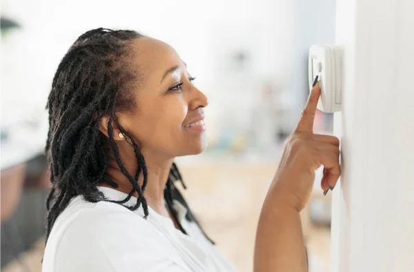 A frican woman lady adjusting the climate control panel on the wall wall thermostat — Stock Photo, Image