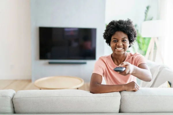 Glad söt kvinna sittande på soffan i ljusa vardagsrum byta TV-kanal — Stockfoto