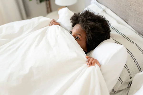Beautiful young African woman in tank top lying in bed cover face with sheet — Stock Photo, Image