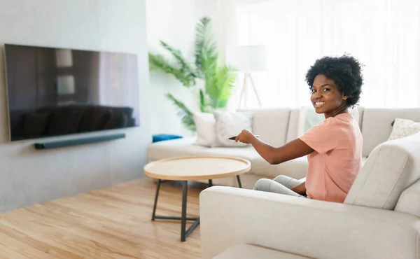 Joyeux femme mignonne assis sur le canapé dans le salon lumineux changer de chaîne de télévision — Photo