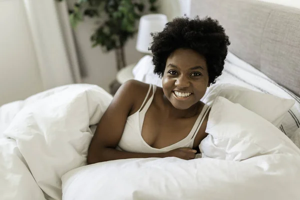 Beautiful young African woman in tank top lying in bed — Stockfoto