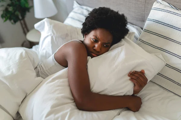 Beautiful young African woman in tank top lying in bed look sad with his pillow — Fotografia de Stock