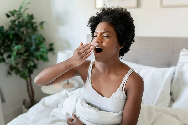 Beautiful young African woman in tank top lying in bed yawn in the morning — Stok Foto