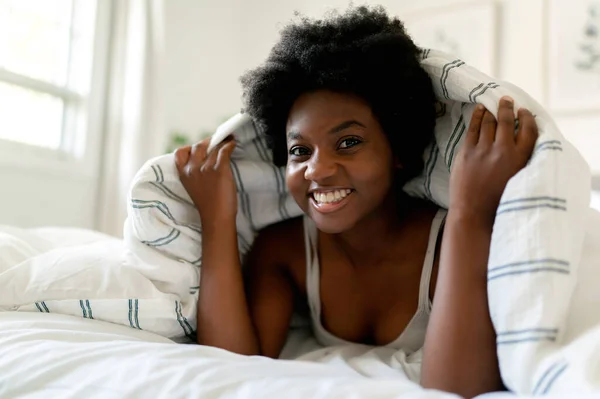 Beautiful young African woman in tank top lying in bed — Stok fotoğraf