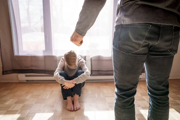 Triest kind jongen zitten op de vloer met vader voor hem met een harde blik en sluit vuist — Stockfoto