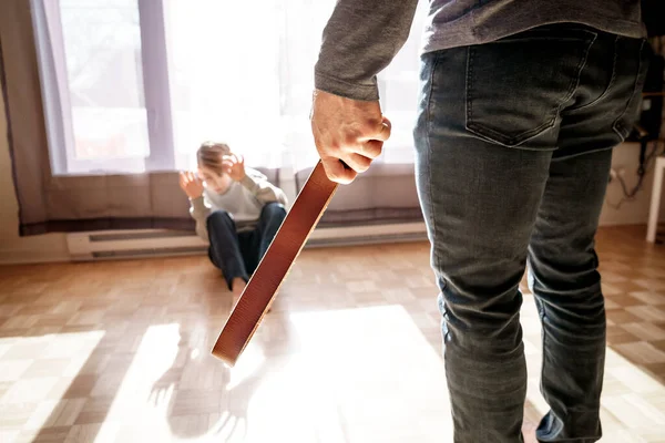 Sorglig pojke sitta på golvet med far framför honom med bälte på handen. — Stockfoto