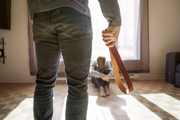 Sorglig pojke sitta på golvet med far framför honom med bälte på handen. — Stockfoto