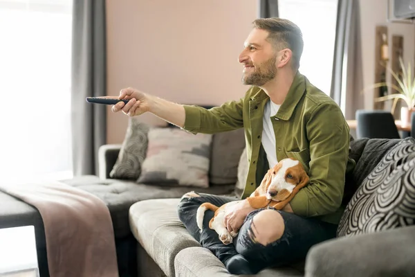 Man Playing With basset Pet Dog At Home sofa listening TV — Foto de Stock