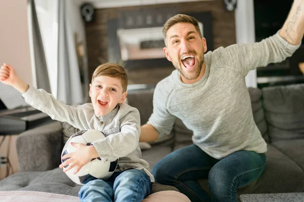 Soccer fans Emotional dad and son cheering with football ball, watching sport on tv at home — Stock Photo, Image