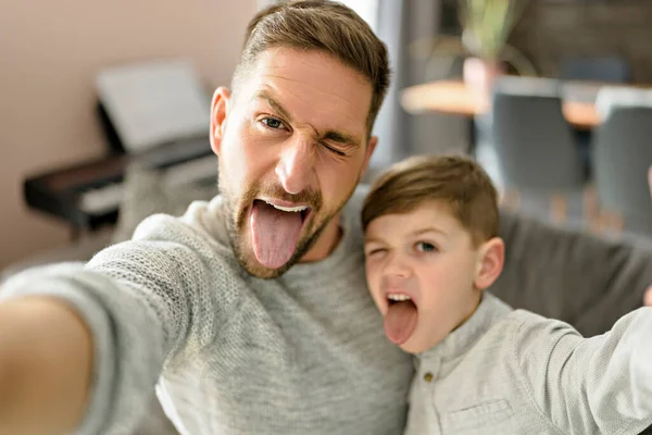 Pai e filho passam tempo juntos no sofá tirando selfies e fazendo caretas — Fotografia de Stock