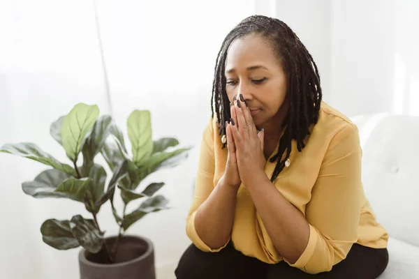 Portrait d'une femme africaine assise sur le canapé et priant Photo De Stock