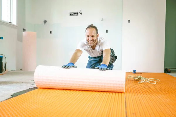Férfi munkavállaló telepíteni narancs tekercs membrán vízszigetelés a padlón — Stock Fotó