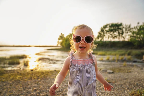 Baby outdoors enjoying nature on the sunset beach with sunglasses — Stock fotografie
