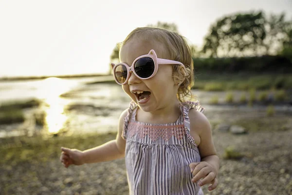 Baby outdoors enjoying nature on the sunset beach with sunglasses — Stock fotografie