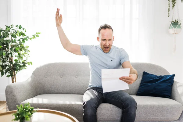 Homem chocado segurando alguns documentos no sofá sala de estar — Fotografia de Stock