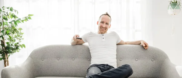 Man with remote control on the sofa at home — ストック写真