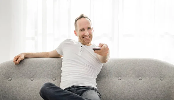 Man with remote control on the sofa at home — Stock fotografie