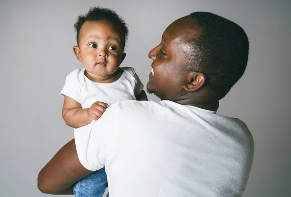 Πορτρέτο του όμορφου αφρικανού άνδρα που κρατά στα χέρια του το μικρό της γιο σε γκρι φόντο — Φωτογραφία Αρχείου