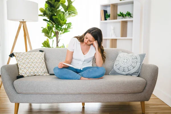 Una chica sentada en un sofá en casa mientras lee los resultados de su reciente prueba de embarazo — Foto de Stock