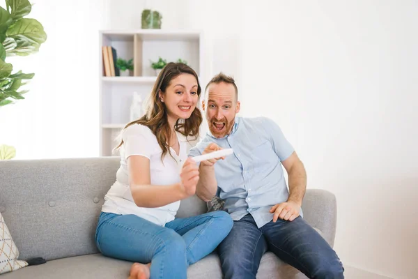 Family happy with pregnancy test with his excited wife sitting on a couch at home. — Photo