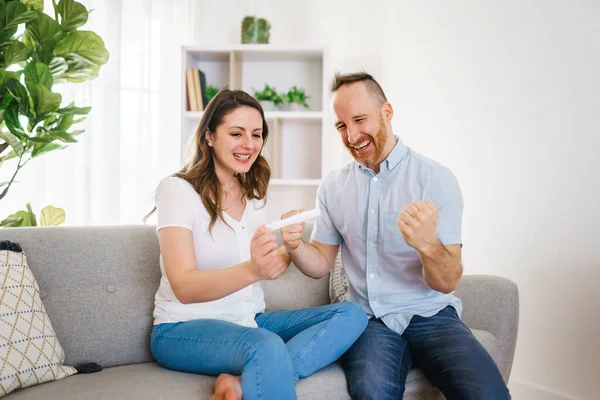 Family happy with pregnancy test with his excited wife sitting on a couch at home. — Foto de Stock