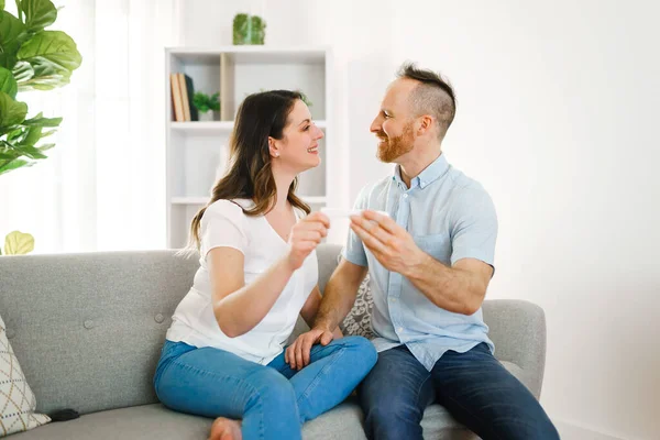 Family happy with pregnancy test with his excited wife sitting on a couch at home. — Foto de Stock