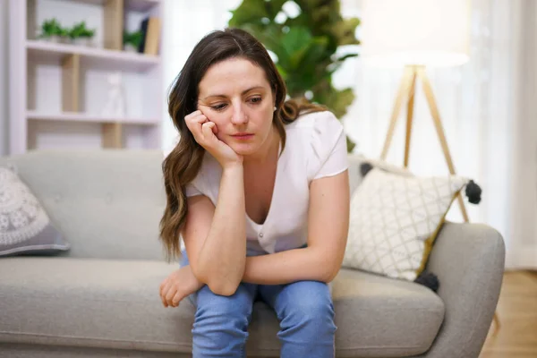 Mujer madura estresada sentada en el sofá en casa mirada triste — Foto de Stock
