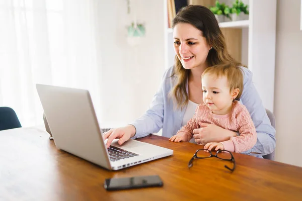 Mor i köket hemmakontor med dator och hennes dotter — Stockfoto