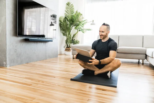 Чоловік на килимку з планшетом робить деякі вправи вдома — стокове фото