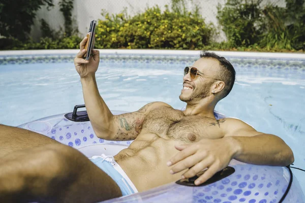 Młody meksykanin i seksowny muskularny mężczyzna pozujący w basenie za pomocą telefonu komórkowego — Zdjęcie stockowe
