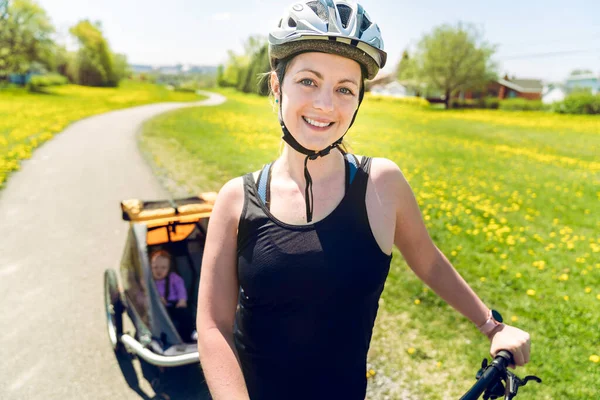 Woman riding a bicycle with a baby stroller attached to the bicycle. — Zdjęcie stockowe