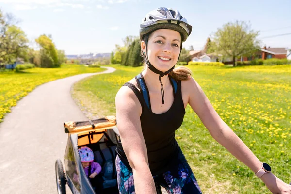 Vrouw rijden een fiets met een kinderwagen bevestigd aan de fiets. — Stockfoto