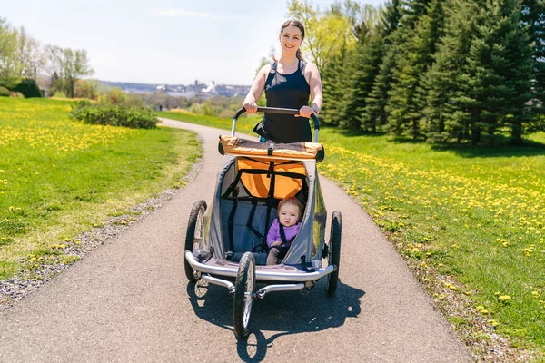 Beautiful young family with baby in jogging stroller running outside in summer season — Stock Photo, Image