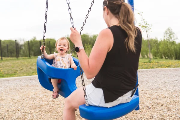 Linda niña jugando en el patio al aire libre con la madre en swing —  Fotos de Stock