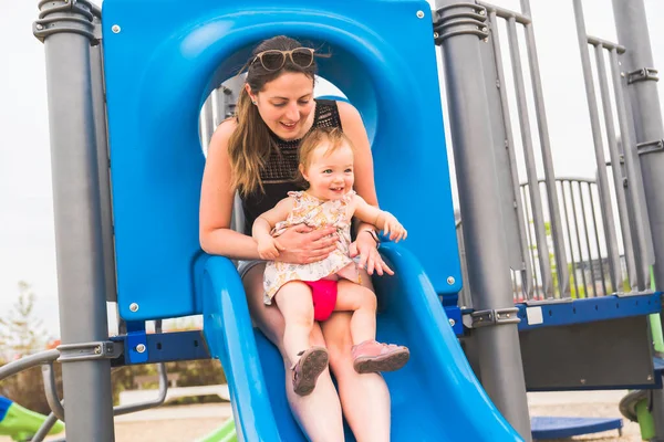 Linda niña jugando en el patio al aire libre con la madre en la diapositiva —  Fotos de Stock