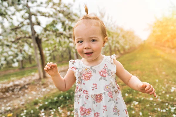 Roztomilé malé usmívající se holčička hraje v kvetoucí jablečné zahradě — Stock fotografie