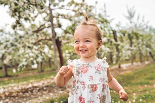 Adorable little smiling baby girl playing in a blooming apple garden — Stock fotografie
