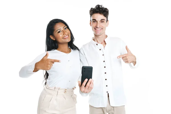 Νεαρό ζευγάρι στέκεται μαζί ποζάρουν στο στούντιο λευκό φόντο κρατώντας κινητό τηλέφωνο και δείχνοντας — Φωτογραφία Αρχείου