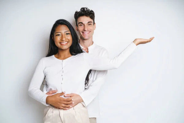 Jong paar staan samen poseren in studio witte achtergrond met de hand tonen iets — Stockfoto