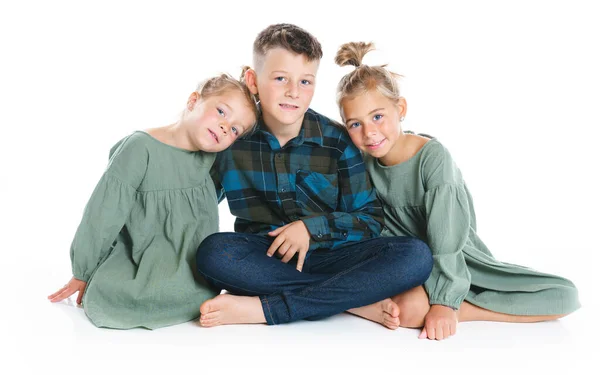 Two cute little sisters with brother on the floor arm in arm cuddling each other in a loving embrace, on white — Foto de Stock