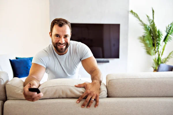 Portrait of smiling man sitting on sofa and watching tv — Foto de Stock