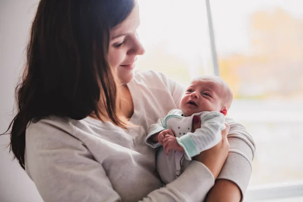 Um bebê recém-nascido em um abraço terno da mãe na janela — Fotografia de Stock