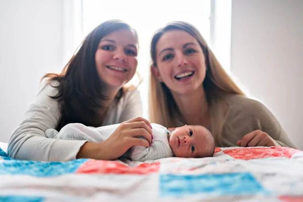 Two friend girl with a newborn baby on bed — Foto Stock