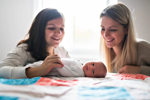 Two friend girl with a newborn baby on bed — Foto de Stock