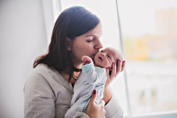 A newborn baby in a tender embrace of mother at window — Foto Stock