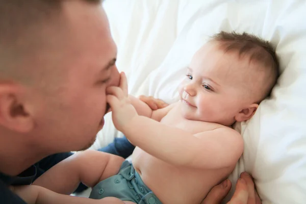 Young father is laying down on a bed and holding is baby. — Foto de Stock